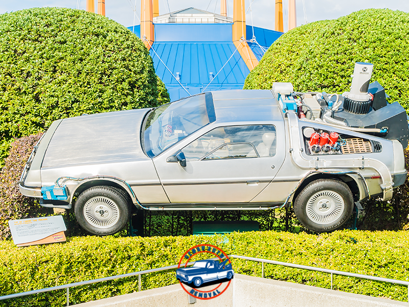 Iconic stainless-steel DeLorean displayed outdoors with detailed futuristic components and trimmed hedges. Valuable Parts in Your Scrap Car