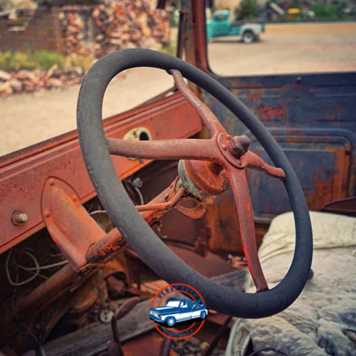 Old rusted car interior with a worn steering wheel and exposed metal parts in a vintage vehicle shell